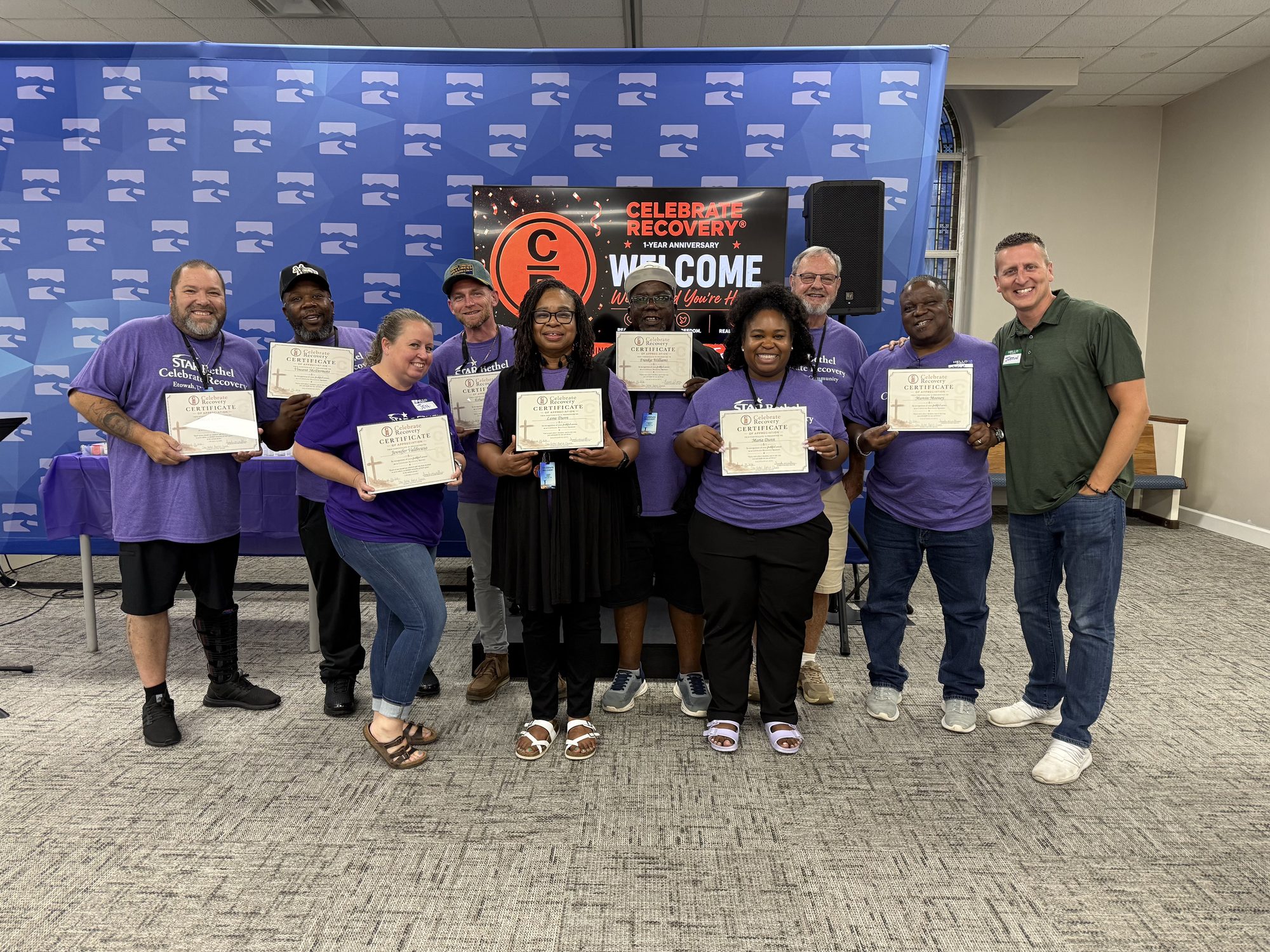 The Star Bethel Celebrate Recovery team in purple shirts holding certificates at the group's one-year anniversary celebration